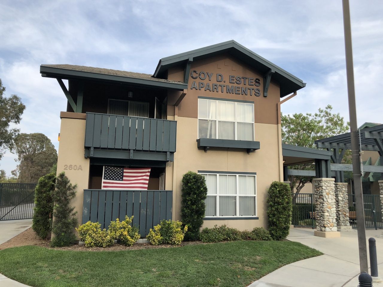 Coy D. Estes Apartments exterior with American flag and landscaped entrance.