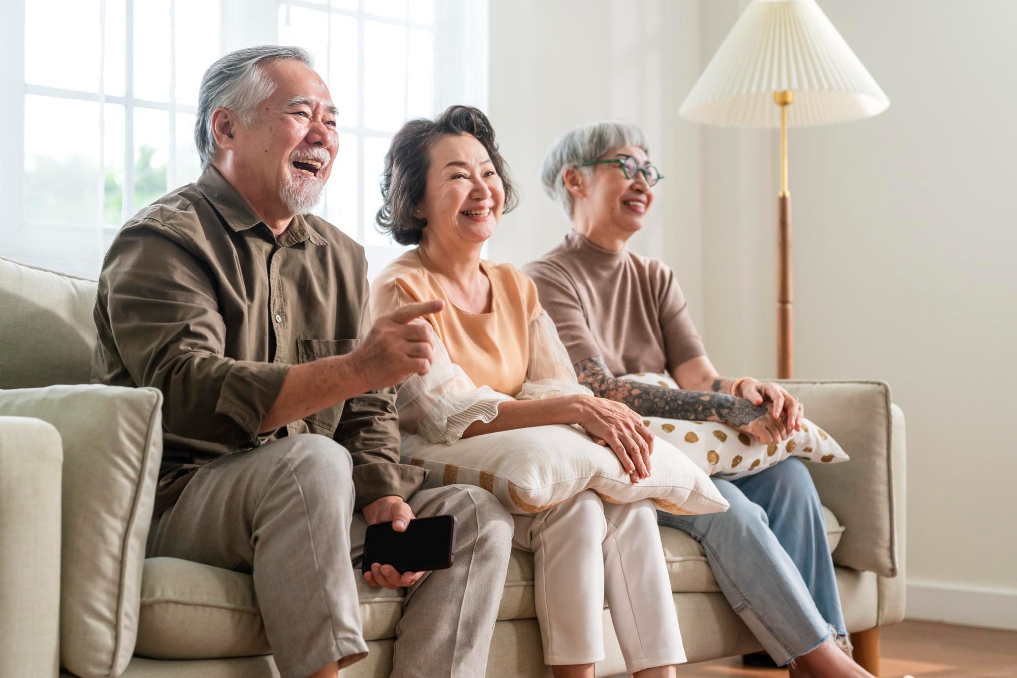 Three senior friends sitting on a couch, laughing together and enjoying each other’s company in a cozy setting.