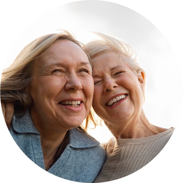 Two senior women smiling joyfully outdoors on a breezy day.